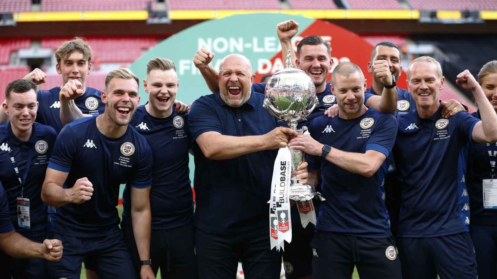 Alan Dunne, right, with Andy Woodman and the Bromley staff celebrating their FA Trophy win in 2022, holding the trophy together