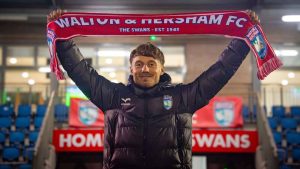 New Walton & Hersham manager Jakub Pietrzak holds aloft a Swans scarf