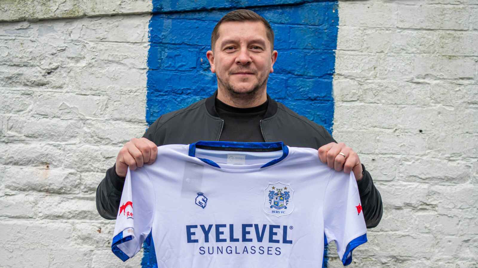 Bury’s new boss Anthony Johnson proudly holds up the club shirt on his first day in charge at Gigg Lane.